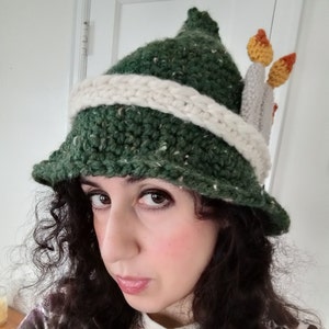 May include: A green crocheted hat with a white brim and orange and yellow crocheted flames on top.
