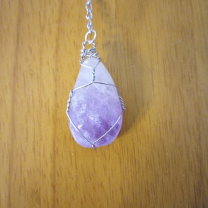 May include: A purple amethyst crystal pendant wrapped in silver wire, hanging from a silver chain.