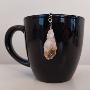 May include: A clear crystal with a yellow center wrapped in silver wire hangs from a black mug.