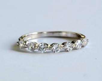 May include: A silver band ring with a row of small, clear round stones set in a curved pattern.