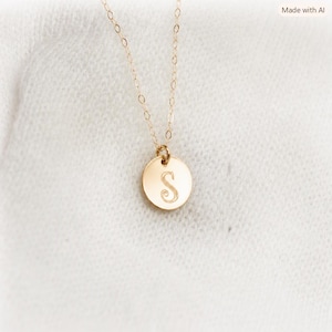 May include: A gold-toned necklace featuring a delicate chain and a small, circular pendant. The pendant is engraved with the uppercase letter S in a classic serif font. The metal has a polished finish that reflects light, creating a bright appearance.