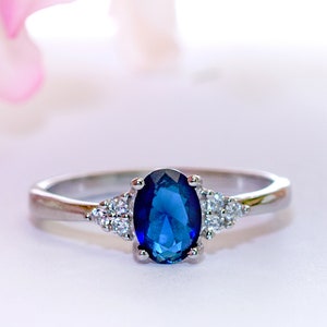 May include: A silver ring with a large oval blue sapphire gemstone and smaller clear gemstones on the band.