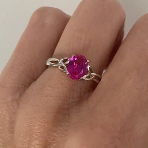 May include: A silver ring with a pink oval-shaped gemstone set in a Celtic knot design.