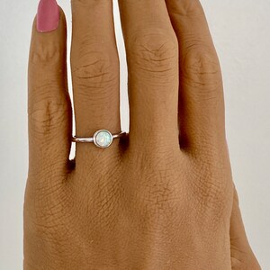May include: A silver ring with a white opal gemstone. The ring is on a person's finger.