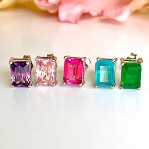 May include: Four pairs of square emerald cut stud earrings in purple, pink, blue, and green.
