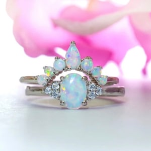 May include: A delicate silver ring set with a large oval opal and smaller opals in a crown-like design.