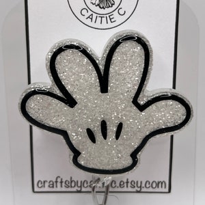 May include: A silver glitter Mickey Mouse hand with black outlines. The hand is attached to a silver clip. The hand is on a white card with black text that reads "Crafts by Caitie" and "craftsbycaitiec.etsy.com".