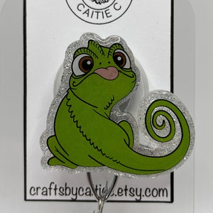 May include: Green glitter chameleon hook with a sparkly silver background. The hook is attached to a white card with the text "Crafts by Caitie" and a flower design.