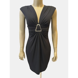 May include: A black dress with a deep V-neckline and cap sleeves. The dress features a gathered design at the waist, accentuated by a silver-colored, triangular embellishment. The dress is displayed on a mannequin.