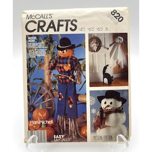 Könnte beinhalten: Ein McCall's Crafts-Muster zum Herstellen von drei Halloween-Dekorationen: einem Vogelscheuche, einem Geist und einem Schneemann. Das Muster heißt "Boo!! Hou!" und ist einfach zu befolgen. Das Muster befindet sich auf einem weißen Hintergrund mit einem roten, schwarzen und weißen Rand.