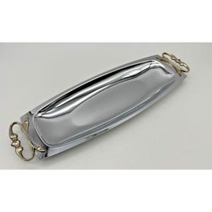 以下が含まれることがあります： 金色の取っ手が付いた、長方形の銀色のサービングトレイ。トレイは、研磨された反射面とわずかに湾曲した形状をしています。ハンドルは装飾的で、装飾的なデザインが施されています。