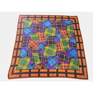 May include: A square scarf featuring a vibrant patchwork of various plaid patterns in shades of blue, green, purple, yellow, and orange. The scarf is framed by a wide border consisting of a black and orange grid pattern that runs along all edges.