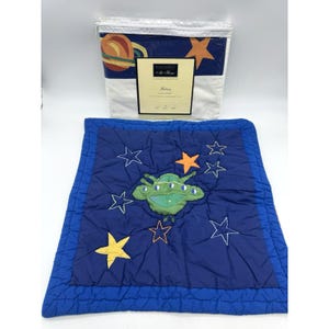 Op de afbeelding: Een blauw-witte platte lakenset met een ruimtethema. De set bevat een plat laken met een planeet- en sterrenontwerp en een blauw gewatteerde kussensloop met een alien- en sterrenontwerp. De set is van de "Galaxy" collectie.