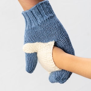 May include: A blue and white knitted mitten with a fingerless design. The mitten is being held by a hand.