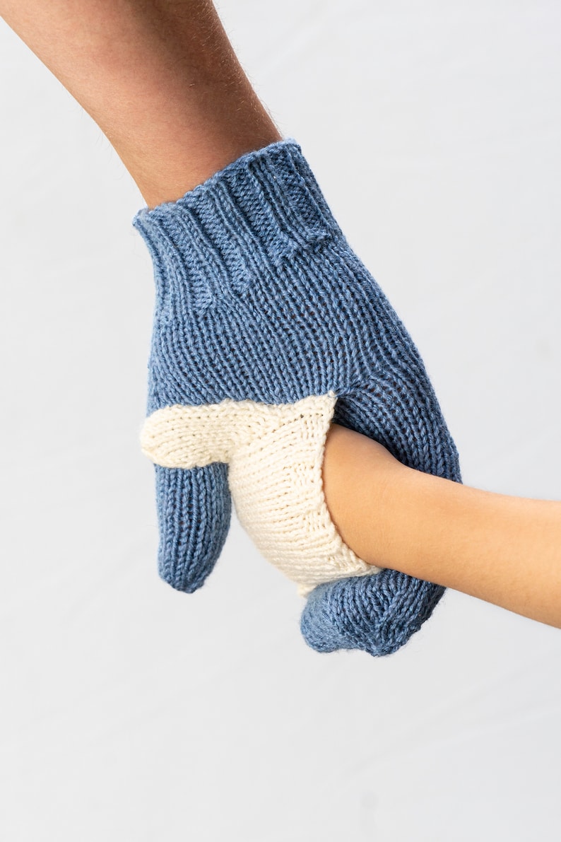 May include: A blue and white knitted mitten with a fingerless design. The mitten is being held by a hand.