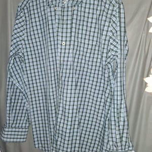 May include: A long-sleeve button-down shirt featuring a plaid pattern in shades of dark green, light blue, and white. The shirt includes a standard collar, a front button placket with light-colored buttons, and buttoned cuffs on the long sleeves.
