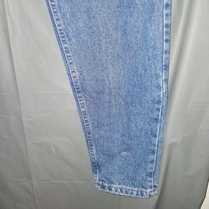 Może przedstawiać: Jasnoniebieskie dżinsy. Dżinsy mają klasyczny pięciokieszeniowy design z prostą nogawką. Denim ma średnie pranie z widocznymi szwami wzdłuż szw&oacute;w. Dżinsy są w stylu casual.