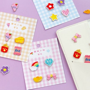 May include: A selection of embroidered patches, including food, flowers, and a diamond, displayed on cards with pink, blue, and tan gingham patterns. Patches include an ice cream cone, cheese, and a bow. Measurements are in centimeters.