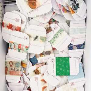 May include: A box filled with various decorative washi tape samples. Each sample is a small, rectangular piece with different designs, including floral, botanical, and patterned motifs. The text "Mini sample" and "ASimpleLifeHandcraft" are visible on the cards.