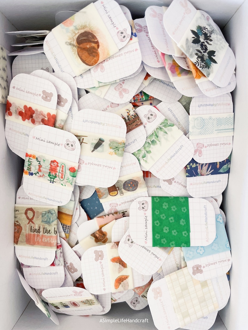 May include: A box filled with various decorative washi tape samples. Each sample is a small, rectangular piece with different designs, including floral, botanical, and patterned motifs. The text "Mini sample" and "ASimpleLifeHandcraft" are visible on the cards.