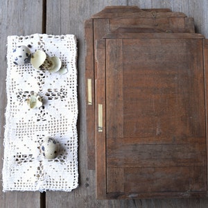 May include: A rustic still life featuring a white lace doily with speckled quail eggs and eggshells, alongside several weathered wooden printing press trays. The scene is set on a wooden surface.