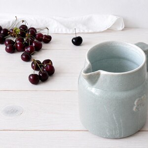 Farmhouse stoneware pitcher styled on white wooden table with cherries