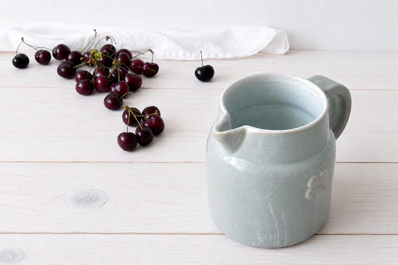 Farmhouse stoneware pitcher styled on white wooden table with cherries