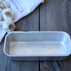 Op de afbeelding: Een rechthoekige, zilverkleurige metalen broodvorm met afgeronde hoeken en een glad binnenoppervlak. De vorm heeft een metallic afwerking en een eenvoudig ontwerp met een open bovenkant, geschikt voor het bakken van brood of ander voedsel.