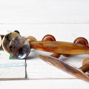 Op de afbeelding: Een collectie meubelbeslag bestaande uit diverse ronde knoppen en twee langwerpige handgrepen, allemaal voorzien van een gemarmerde, doorschijnende amber- en bruinkleurige harsafwerking met zichtbare metalen bevestigingsstelen.