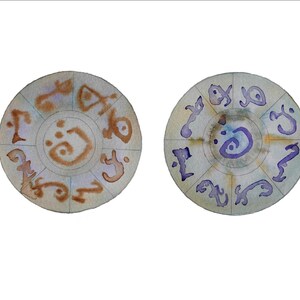 May include: Two circular watercolour paintings with a mandala design. The first painting is brown with a light blue background. The second painting is purple with a light green background.