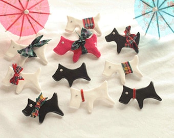 May include: A collection of nine ceramic dog figurines, each with a different color and pattern. The dogs are all in a sitting position with their tails curled up. Some of the dogs have plaid bows, while others have solid color bows.