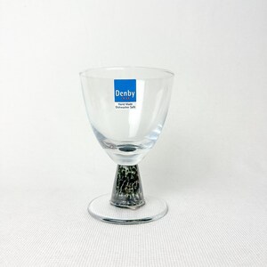 May include: A clear glass goblet with a textured, dark green and black base and a round clear base. The goblet has a blue sticker that reads "Denby" and "Hand Made Dishwasher Safe".
