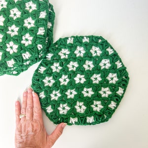 May include: Three crocheted coasters in green and white with a flower pattern. The coasters are stacked on top of each other.