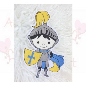 Könnte beinhalten: Gestickter Aufnäher eines Cartoon-Ritters. Der Ritter trägt einen silbernen Helm mit gelber Feder, silberne Rüstung und einen blauen Umhang. Er hält einen gelben Schild mit blauem Kreuz. Der Aufnäher hat einen weißen Rand.