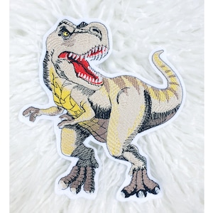 Könnte beinhalten: Gestickter Aufnäher mit einem Tyrannosaurus Rex Dinosaurier. Der Aufnäher hat einen beigefarbenen Körper mit braunen Streifen, gelben Akzenten und einem roten Maul. Der Dinosaurier wird in einer stehenden Pose mit offenem Maul dargestellt.