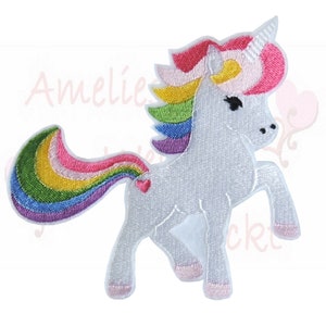 Könnte beinhalten: Gestickter Aufnäher eines weißen Einhorns mit Regenbogenmähne und -schwanz. Das Einhorn hat ein rosa Herz an der Flanke. Der Text "Amelie's pocket" ist im Hintergrund sichtbar. Weißer Hintergrund.