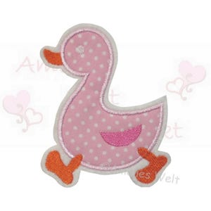 Könnte beinhalten: Ein rosa Enten-Applikation mit weißen Tupfen und orangefarbenen Akzenten. Die Ente ist weiß umrandet und hat einen rosa Bauch. Die Applikation ist so gestaltet, dass es aussieht, als würde die Ente laufen.