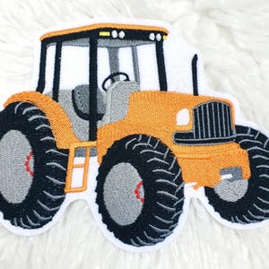 Könnte beinhalten: Gestickter Aufnäher eines orangefarbenen Traktors mit schwarzen Reifen und einer grauen Kabine. Der Traktor hat eine weiße Umrandung und detaillierte Nähte. Die Räder haben rote Akzente. Geeignet für Kleidung oder Bastelprojekte.