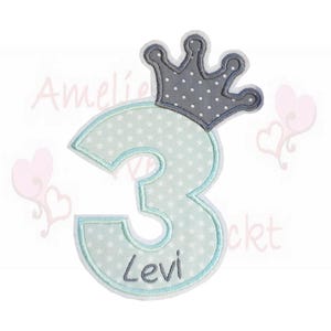 Könnte beinhalten: Hellblaue Applikation mit der Zahl 3 und einer Krone, Sternmuster und dem Namen "Levi". Die Krone ist grau mit weißen Punkten. Die Applikation ist wahrscheinlich für eine Geburtstagsfeier.