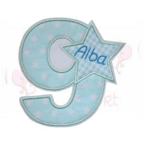 Könnte beinhalten: Hellblaue Applikation der Zahl 9 mit weißem Sternmuster und einem Vichy-Stern mit dem Namen "Alba" in Blau gestickt. Die Applikation hat eine weiße Rückseite und eine genähte Bordüre.