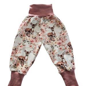 Könnte beinhalten: Weiße Babyhose mit Blumen- und Hirschdruck. Die Hose hat einen rosa elastischen Bund und Bündchen.