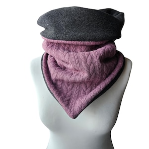 Könnte beinhalten: Ein zweifarbiger Halswärmer mit Zopfmuster. Der obere Teil ist dunkelgrau und der untere Teil ist mauvefarben. Der Halswärmer wird auf einer weißen Schaufensterpuppe präsentiert. Die Kanten sind mit einem dunkelgrauen Rand versehen.
