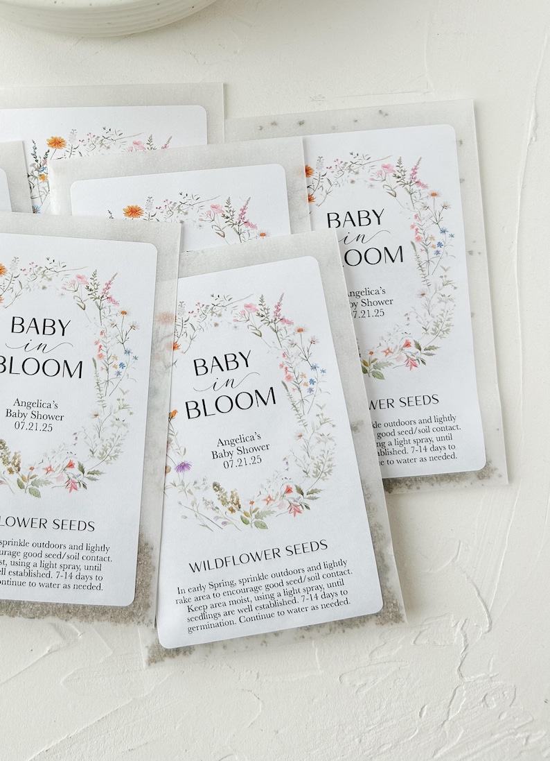 May include: A set of white envelopes with floral designs and the text "Baby in Bloom" and "Angelica's Baby Shower 07.21.25". Each envelope contains wildflower seeds and instructions for planting.