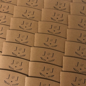 May include: A stack of brown paper coffee cup sleeves with the initials "J&J" and a small heart printed on each sleeve.