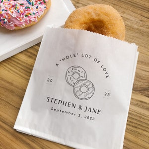 May include: A white paper bag with a donut design and the text "A "HOLE" LOT OF LOVE" and "STEPHEN & JANE September 2, 2023".