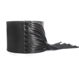 Op de afbeelding: Zwarte leren armband met een franje detail. De armband is gestikt met een decoratieve naad.