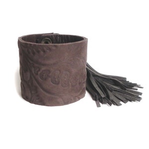 May include: A brown leather cuff bracelet with a paisley pattern and a black leather tassel.