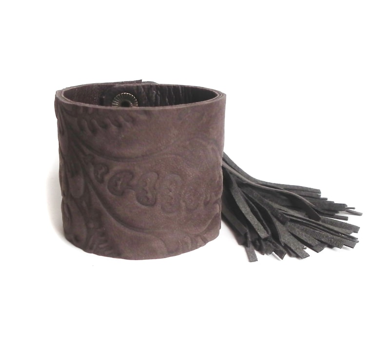 May include: A brown leather cuff bracelet with a paisley pattern and a black leather tassel.