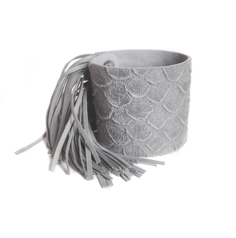 May include: Gray leather bracelet with a fringe tassel. The bracelet has a textured, scaly design.