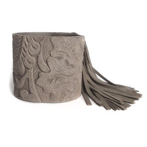 May include: A gray suede bracelet with a tassel. The bracelet has an embossed floral pattern.